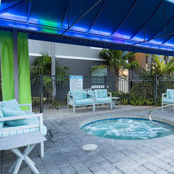 a patio with a hot tub and chairs under a blue canopy.