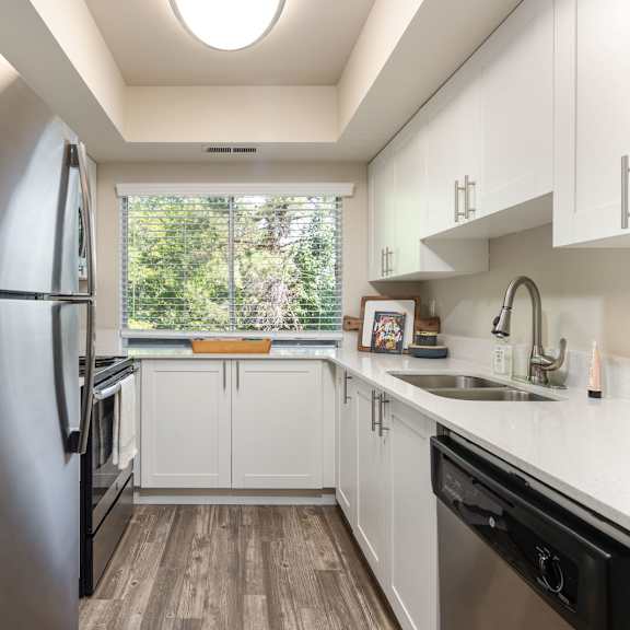 a white kitchen with stainless steel appliances and a window