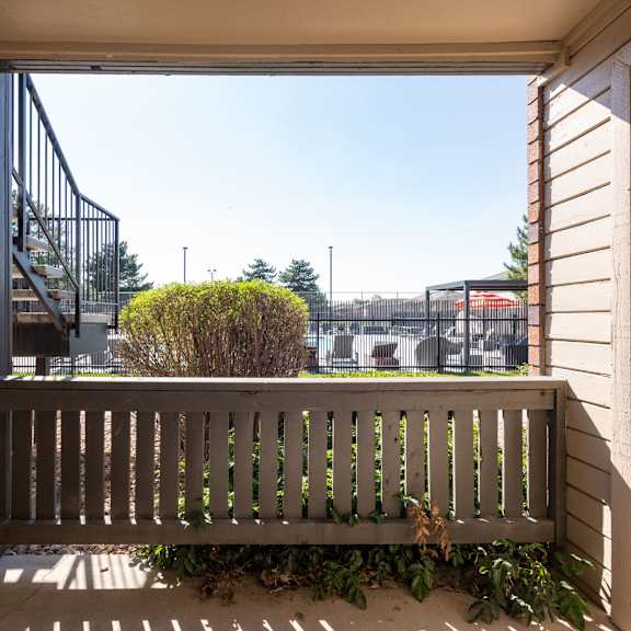 a balcony with a wooden bench and a view of a building and a playground