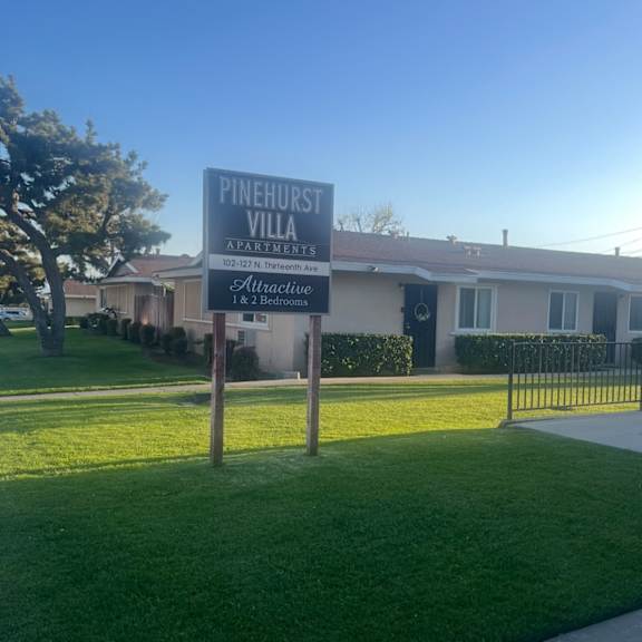 a sign for pinehurst villa apartments stands in front of a building.