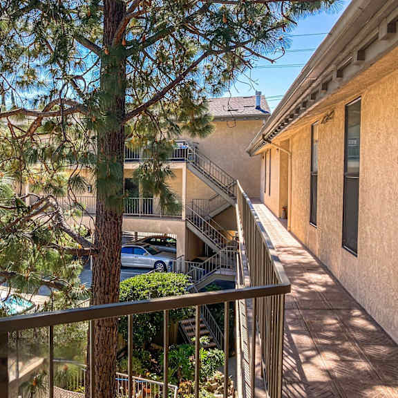 a balcony with a railing overlooks a tree and a car.