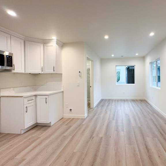 a spacious kitchen with white cabinets and a wooden floor.