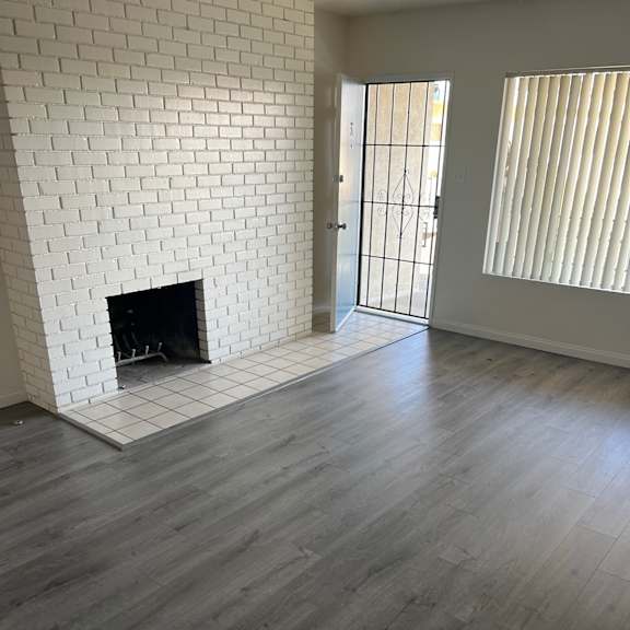 a room with a white brick fireplace and wooden flooring.
