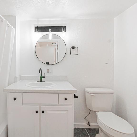 a white bathroom with a toilet, sink, and mirror.