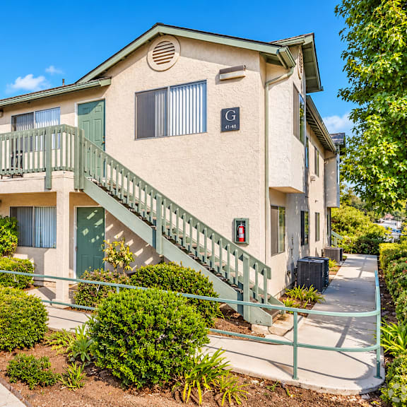 a beige building with a green railing and bushes in front.