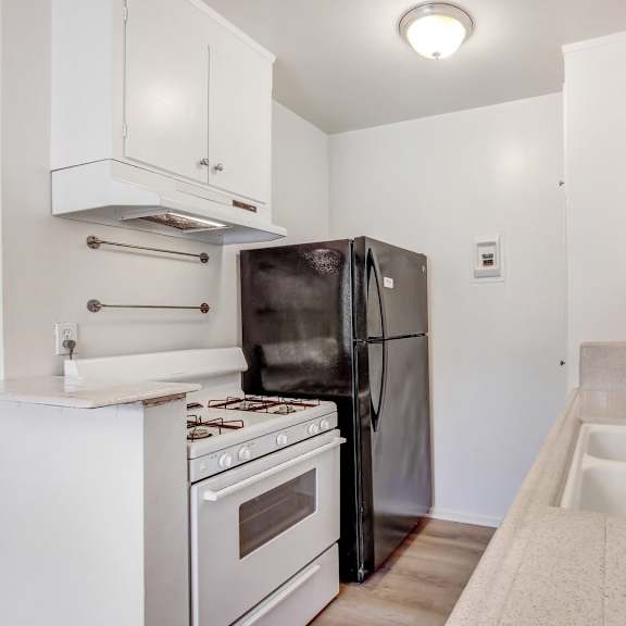 a kitchen with a black refrigerator, white cabinets, a stove, and a sink.