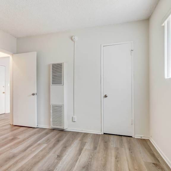 a room with white walls and wooden flooring with a white door on the left and a white wardrobe on the right.