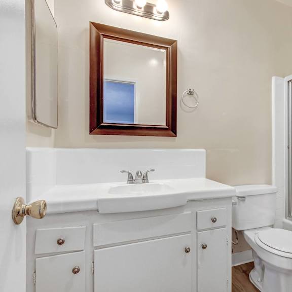 a white bathroom with a toilet, sink, and mirror.