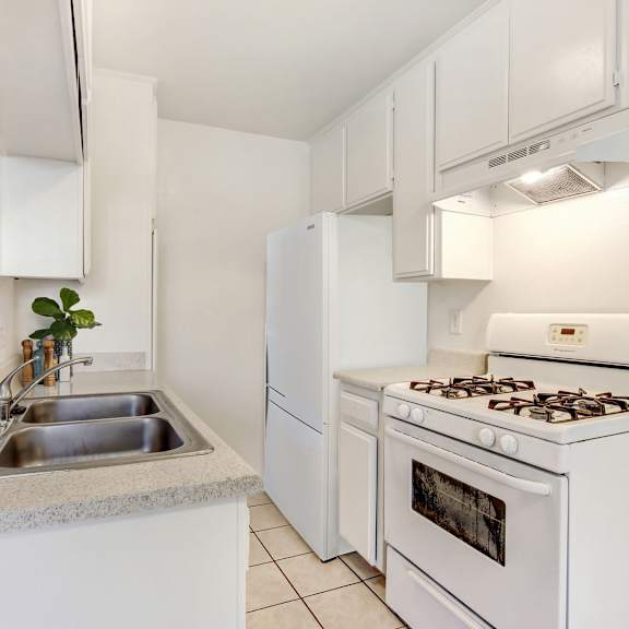 a white kitchen with a stove, sink, and cabinets.