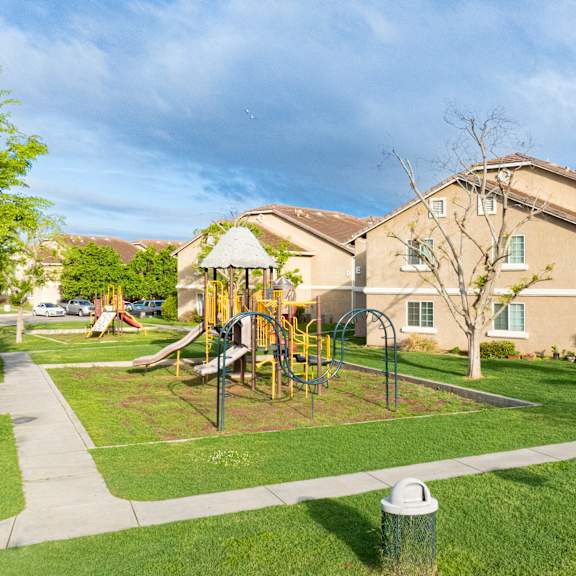 a playground with a slide and swings is in front of a building.