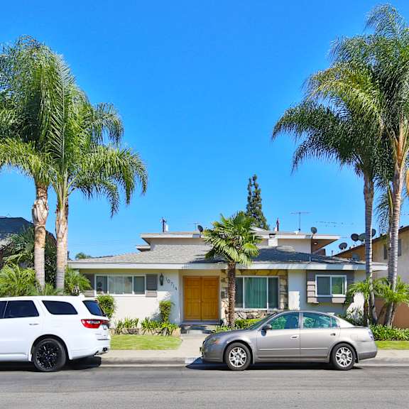 two cars are parked in front of a house with palm trees.