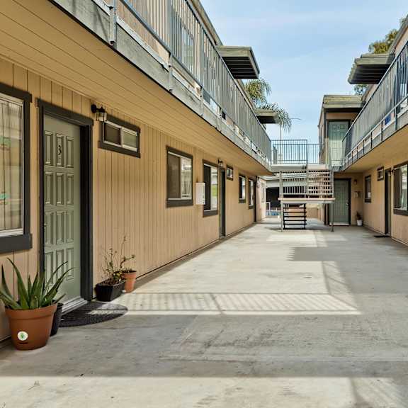 a long hallway with doors on both sides and potted plants on the floor.