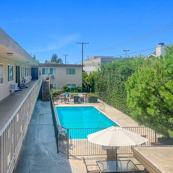 a pool with a sun lounger and umbrella is surrounded by a fence.