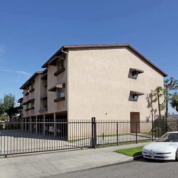 a white car is parked in front of a beige building with a black fence.