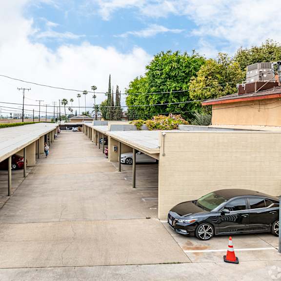 a black car is parked in a parking lot with a green hedge on the left.