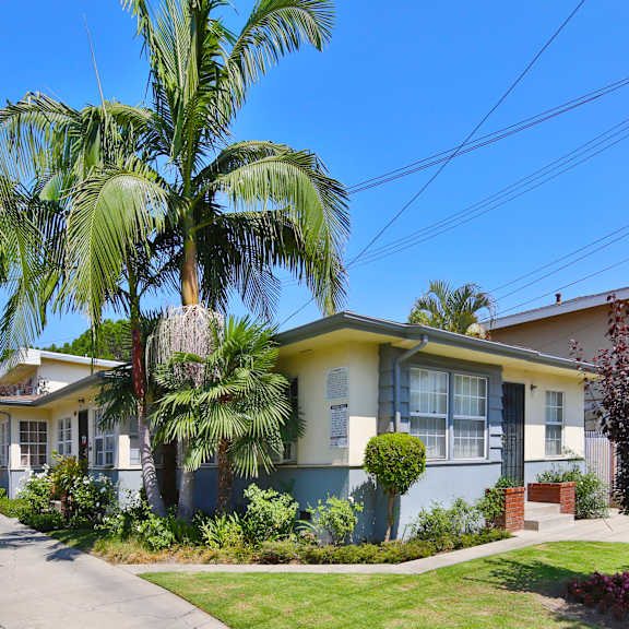 a house with a blue and yellow facade is surrounded by greenery and a clear blue sky.