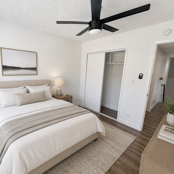 a bedroom with a large bed, a ceiling fan, and a small nightstand with a lamp.