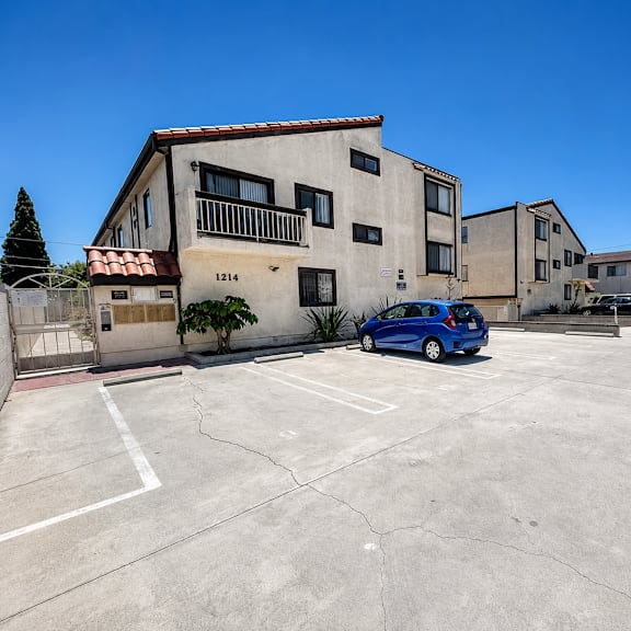 a blue car is parked in a parking lot in front of a building with the number 1214 on it.