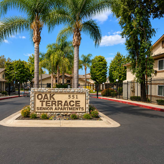 a sign for oak terrace senior apartments is in the foreground of a tree-lined street.