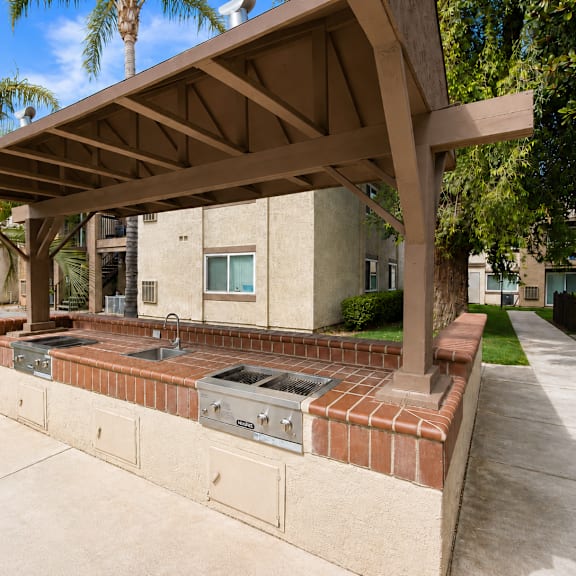 a covered outdoor kitchen area with a grill and sink.