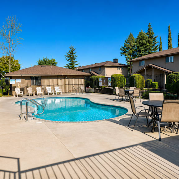 a pool surrounded by chairs and a table with a house in the background.