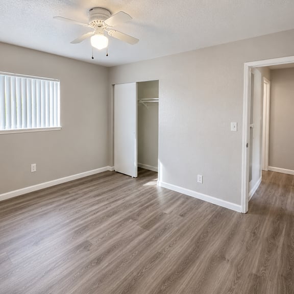 a room with a ceiling fan and light, hardwood floors, and a window with blinds.
