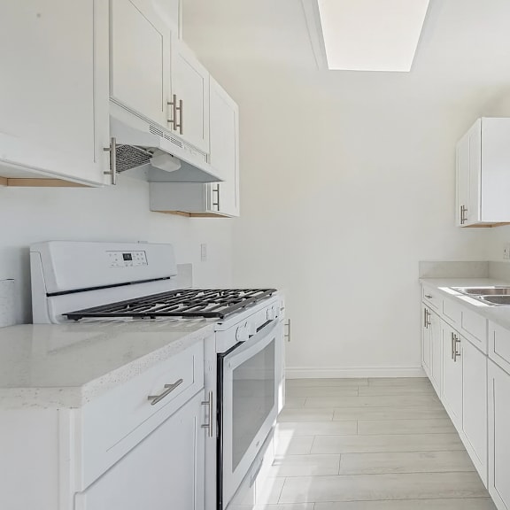 a white kitchen with a stove, sink, and cabinets.