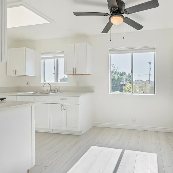 a white kitchen with a ceiling fan and a window.