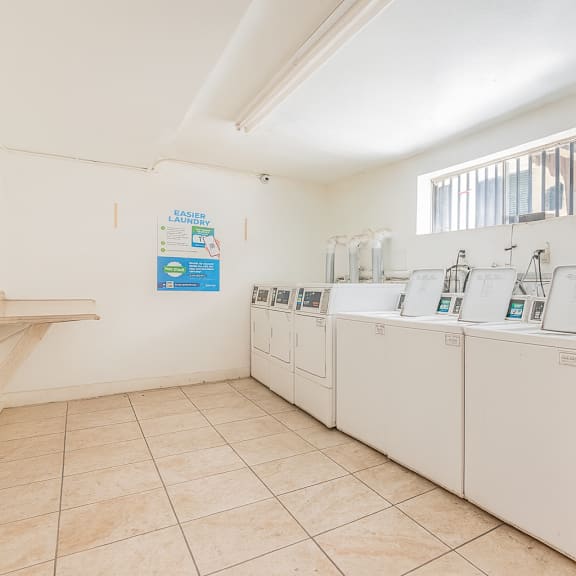 a room with a white wall and a row of washing machines.