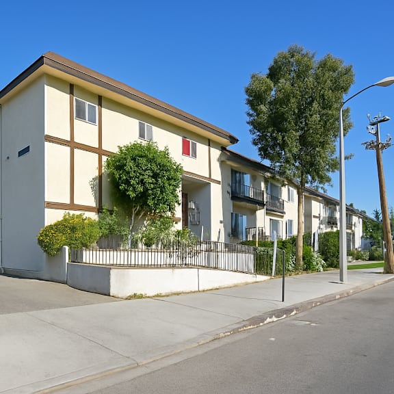 a building with a white facade and a yellow roof is surrounded by a fence and has a tree in front of it.