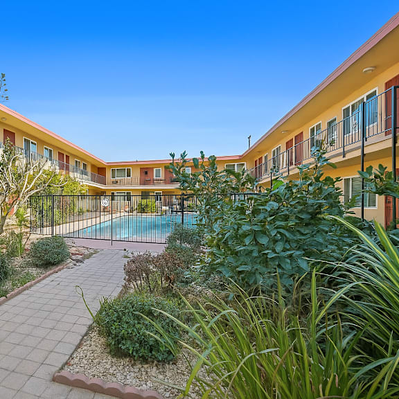 a sunny day at a residential complex with a pool and a well-maintained garden.