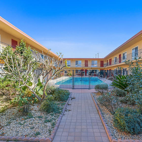 a courtyard with a pool surrounded by plants and buildings with red and yellow balconies.