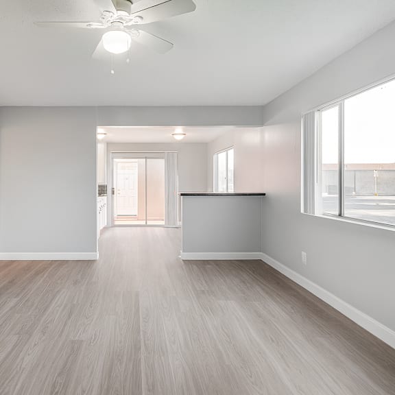 a spacious room with a ceiling fan and light, hardwood flooring, and a large window with blinds.