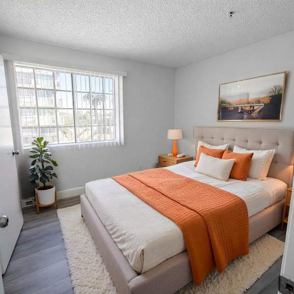 a bedroom with a bed, orange blanket, and a painting on the wall.