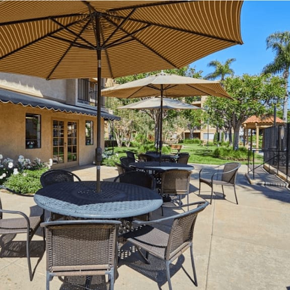 a patio with tables and umbrellas in front of a building at huntington terrace north senior, huntington beach, ca