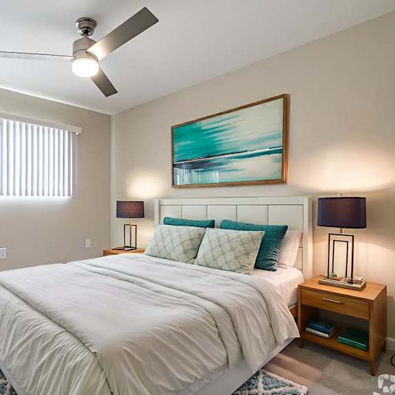a bedroom with a large bed, a ceiling fan, and a painting on the wall.