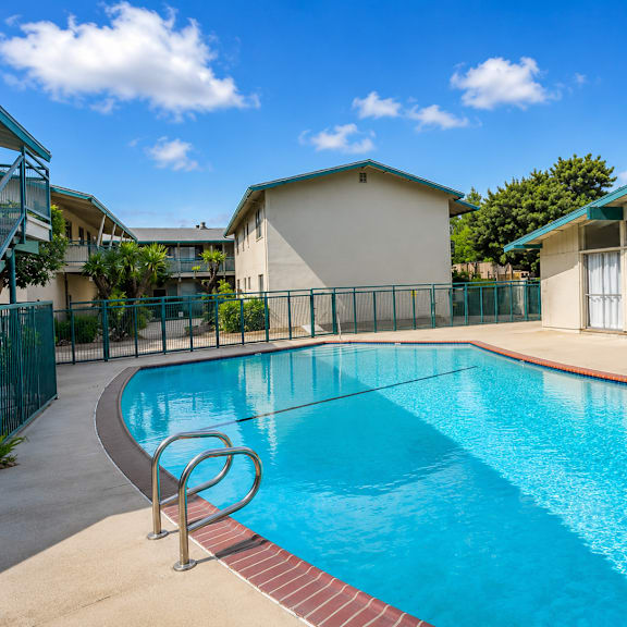a swimming pool surrounded by a fence and a building in the background.