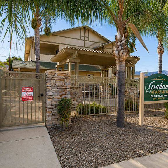 a sign for graham apartments is in front of a building with a fence and palm trees.