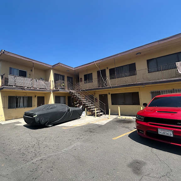 a red car is parked in a lot in front of a building.