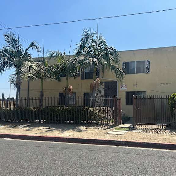 a building with a fence and palm trees in front.