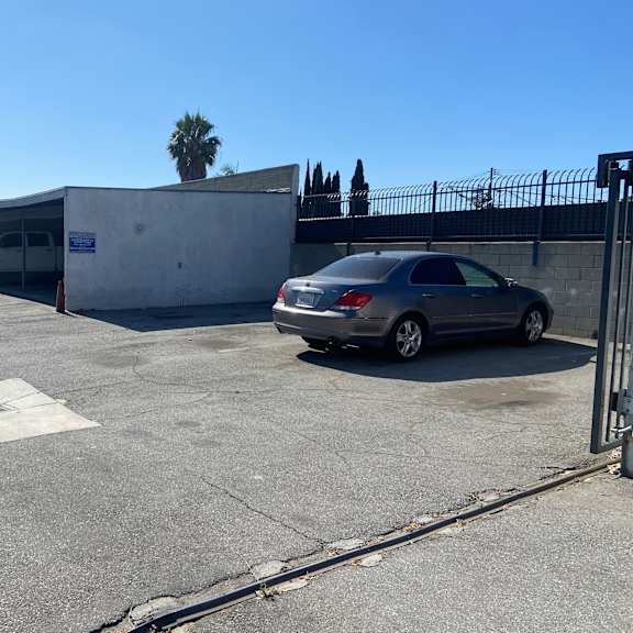 a car is parked in a parking lot with a white building and a fence in the background.