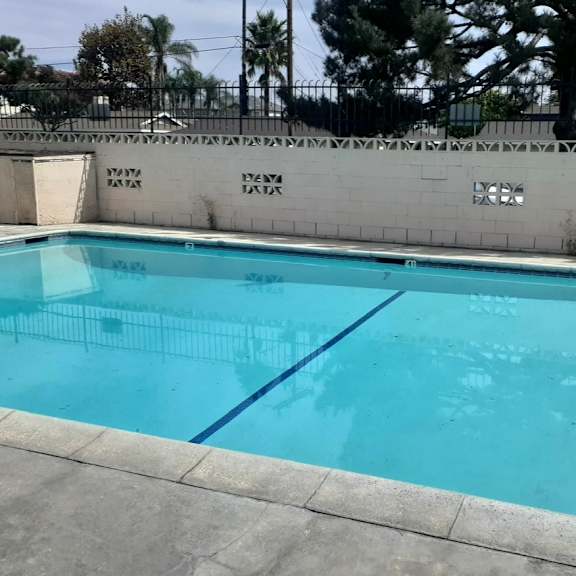a rectangular pool with a blue tiled edge and a white fence around it.