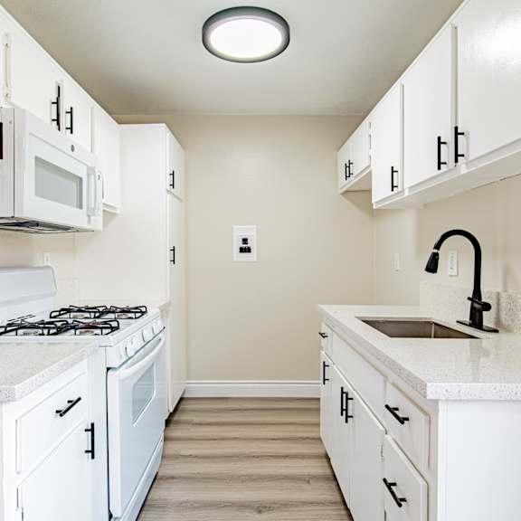 a white kitchen with a stove, microwave, and sink.