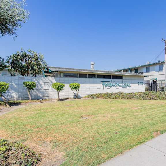 a building with a wall covered in graffiti is surrounded by a green lawn and palm trees.