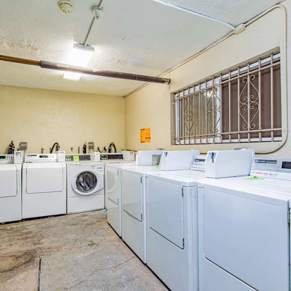 a row of white front load washing machines are lined up in a laundry room.