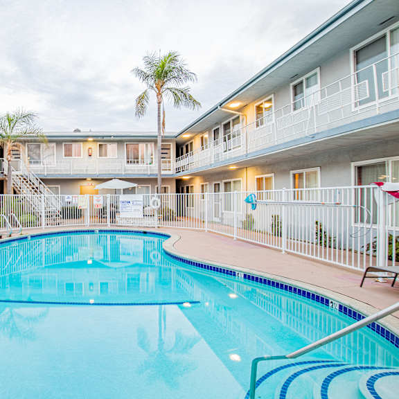 a large swimming pool in a resort with a white building in the background.
