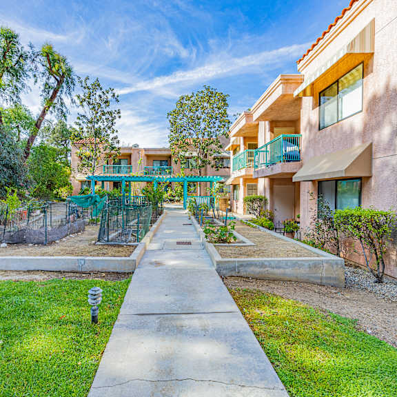 a sunny day at a residential area with apartment buildings and a green fence.