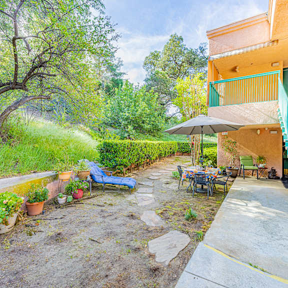 a patio with a table and chairs is surrounded by a green railing and a tree.