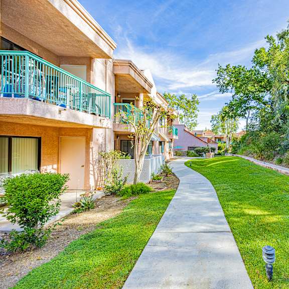 a concrete walkway leads through a grassy area between two apartment buildings.