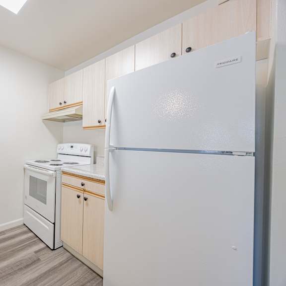 a white refrigerator stands in a kitchen with wooden cabinets and a stove.
